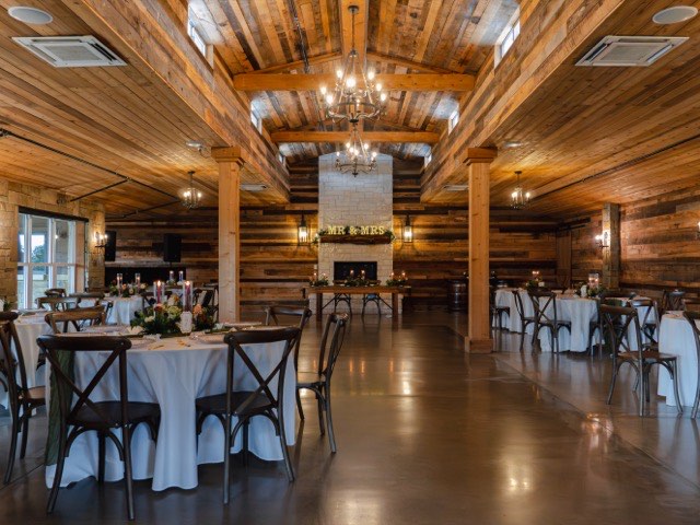 Reception setup at The Melissa Barn with dressed tables, wooden chairs and a central aisle toward the fireplace